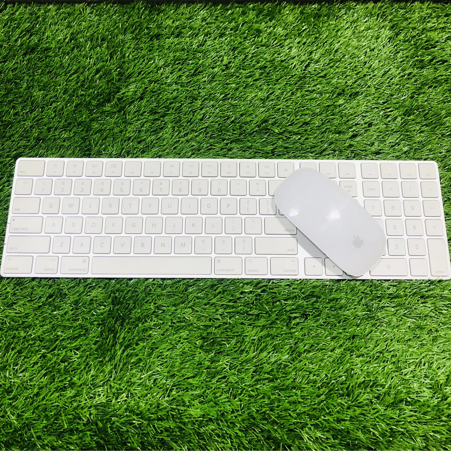 White keyboard and mouse set on green grass with a dark green fabric background